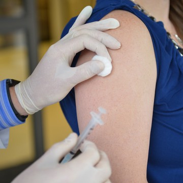 A close-up image of an arm with a rolled-up sleeve, ready to receive a vaccine injection. In the foreground, a syringe filled with vaccine is visible, held by a healthcare professional's gloved hand. The background may feature a sterile medical environment, such as a clinic or vaccination center. This image depicts the readiness for administering a vaccine, highlighting the importance of immunization in public health efforts