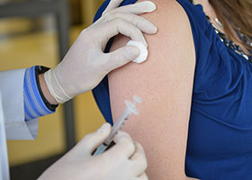 A close-up image of an arm with a rolled-up sleeve, ready to receive a vaccine injection. In the foreground, a syringe filled with vaccine is visible, held by a healthcare professional's gloved hand. The background may feature a sterile medical environment, such as a clinic or vaccination center. This image depicts the readiness for administering a vaccine, highlighting the importance of immunization in public health efforts.